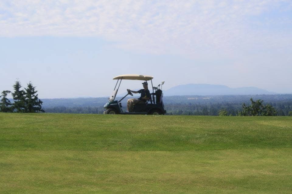A golfer riding the back nine with distant Northwest views